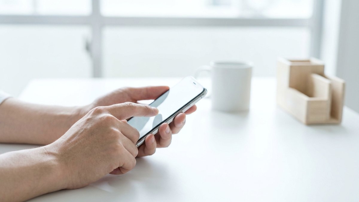 明るい部屋でスマートフォンを手に持ち、問い合わせフォームを入力している手元