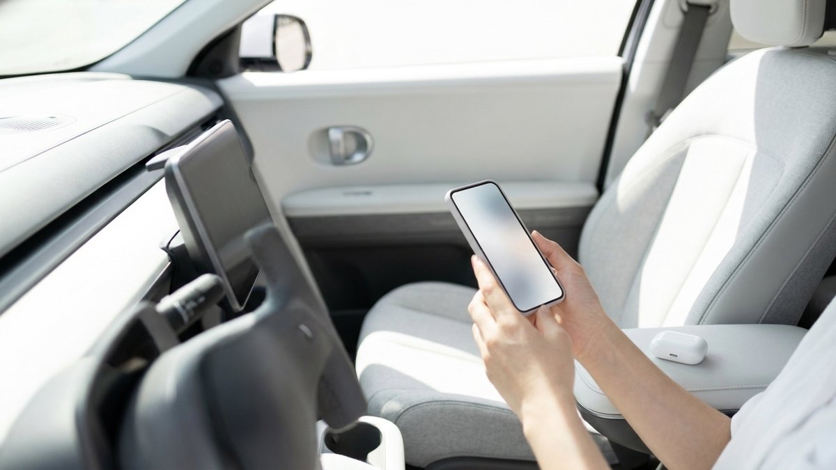 明るい車内でスマートフォンを手に持ち、音声を聴こうとしている人の手元